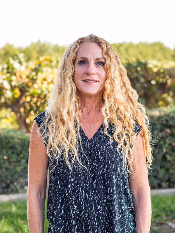Carol E. Franzia smiling and standing in front of trees