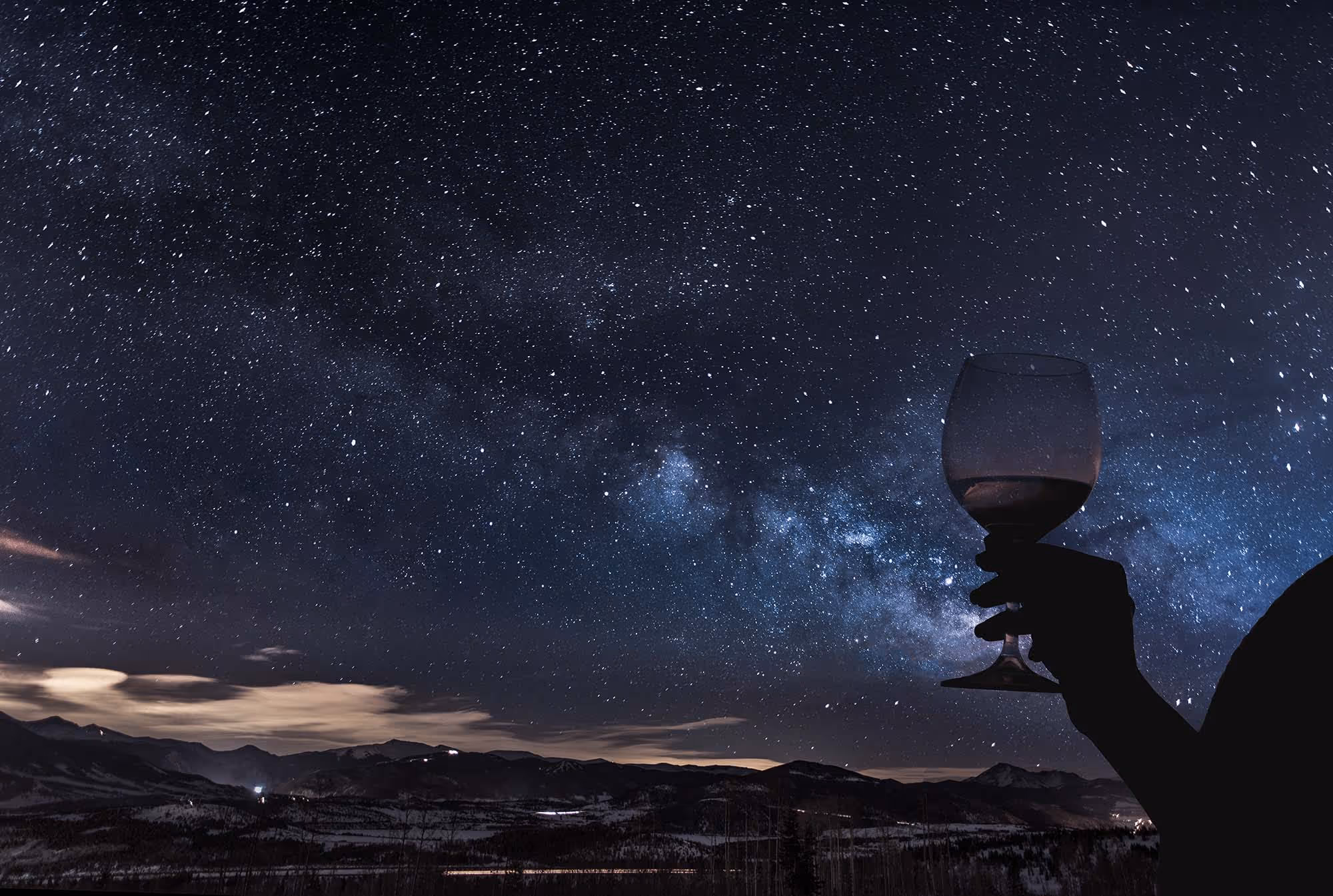 A hand holding a wine glass in front of a starry night sky