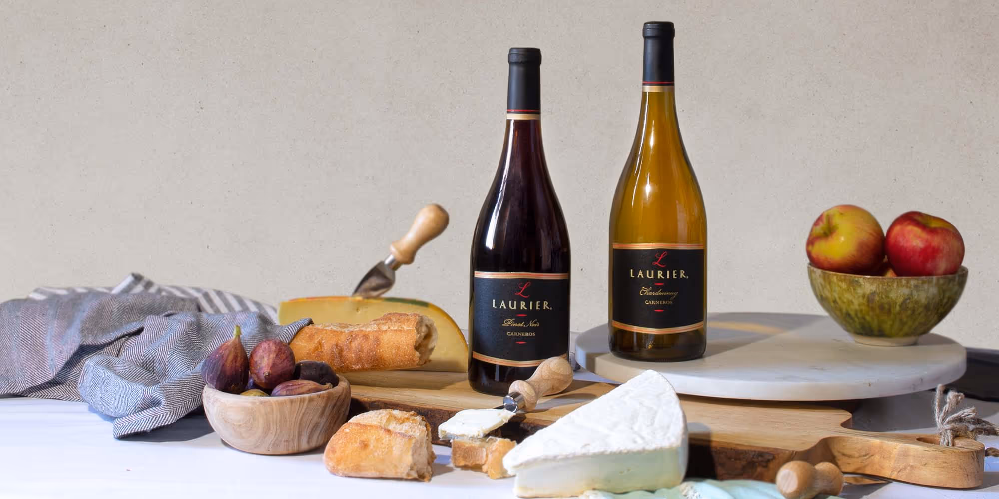 Bottles of Laurier Pinot Noir and Chardonnay on cutting boards next to bread and fruits