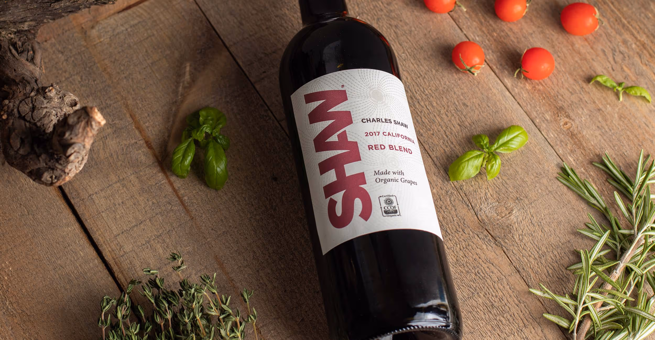 A bottle of Shaw Organic Red Blend on a wooden table with herbs and tomatoes