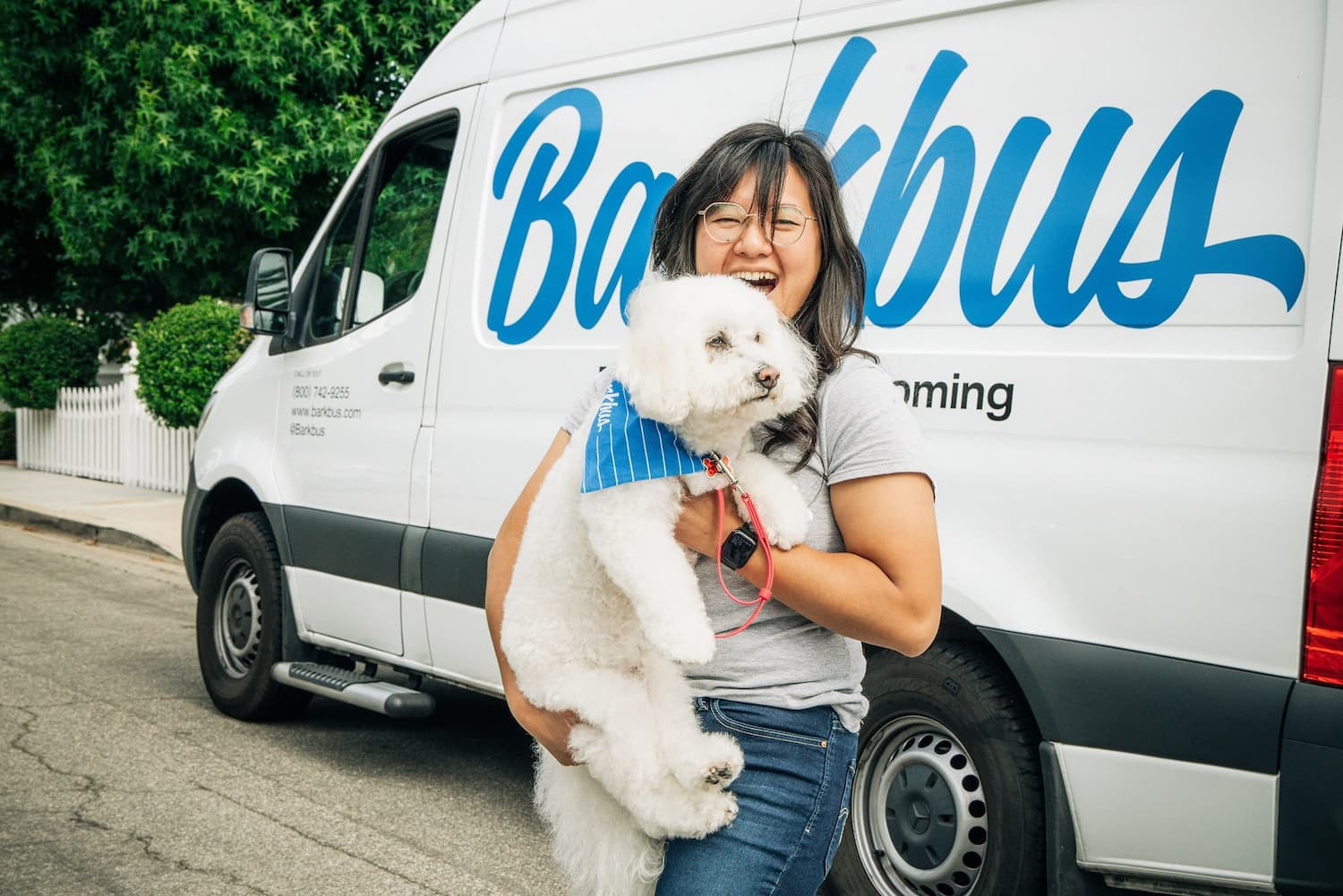 groomer with white dog standing in front of barkbus van