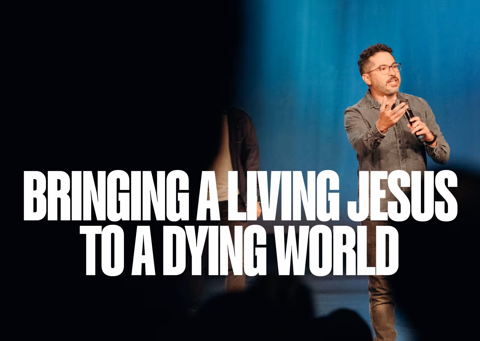 Man speaking on stage with microphone, with text 'Bringing a living Jesus to a dying world' overlayed.