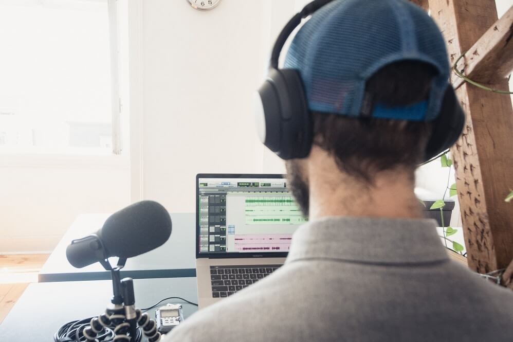 Man recording a podcast remotely with a laptop, microphone and headphones.