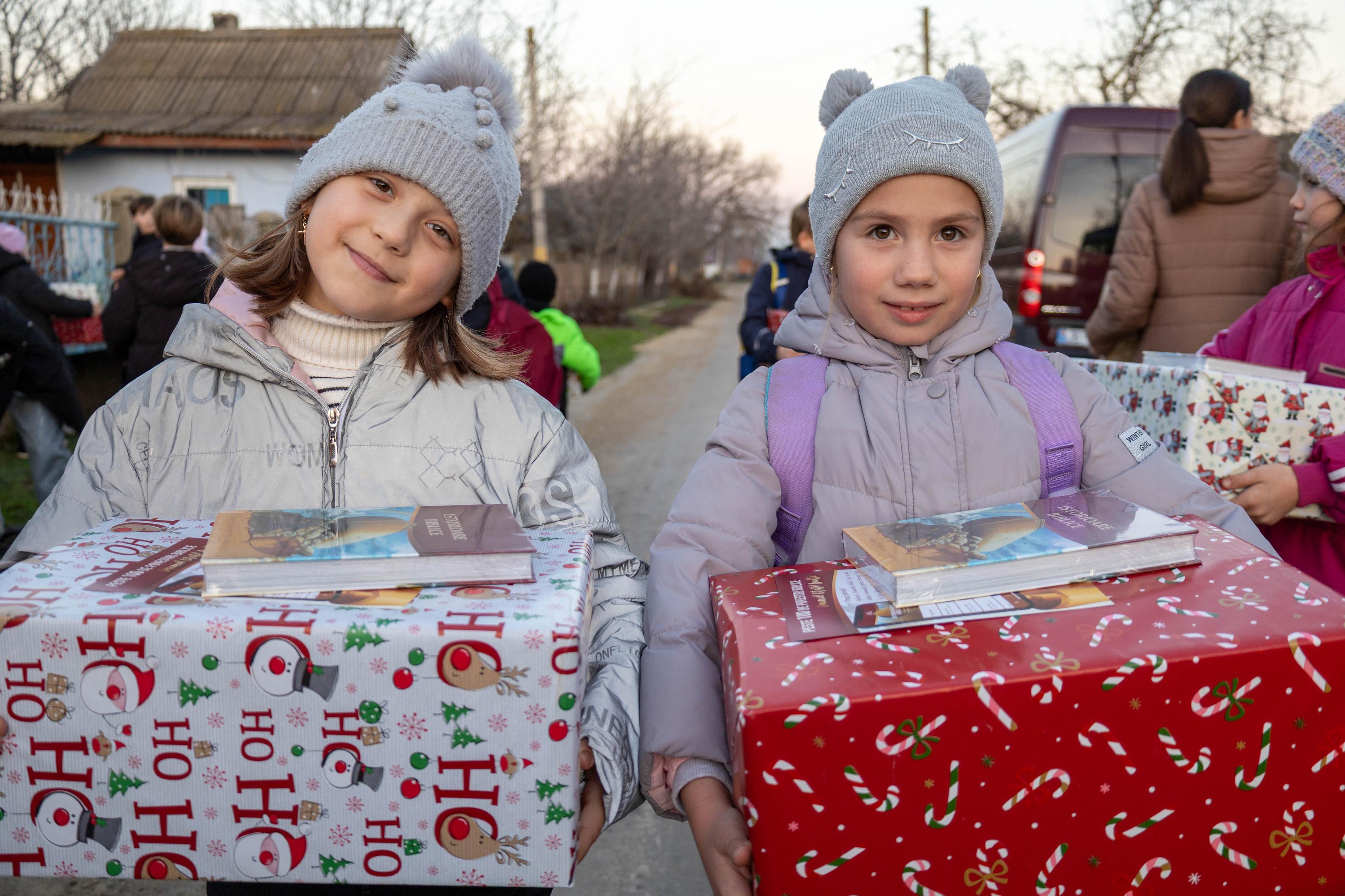 Zwei Kinder halten Weihnachtspakete und Bibeln in der Hand 