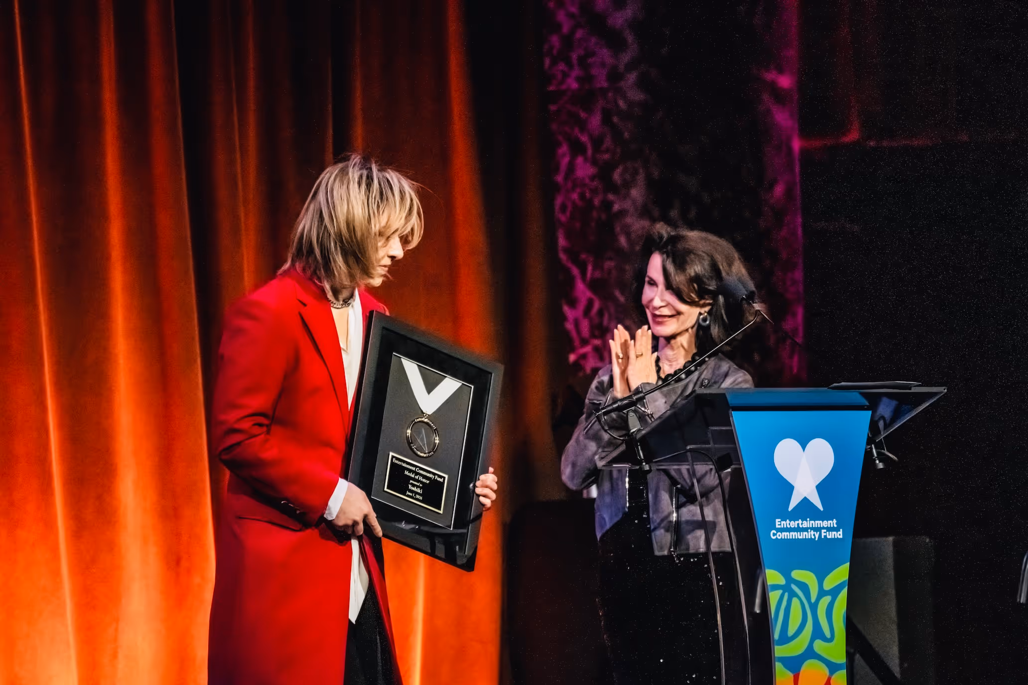 YOSHIKI  in red coat receiving award at the Entertainment Community Fund event.
