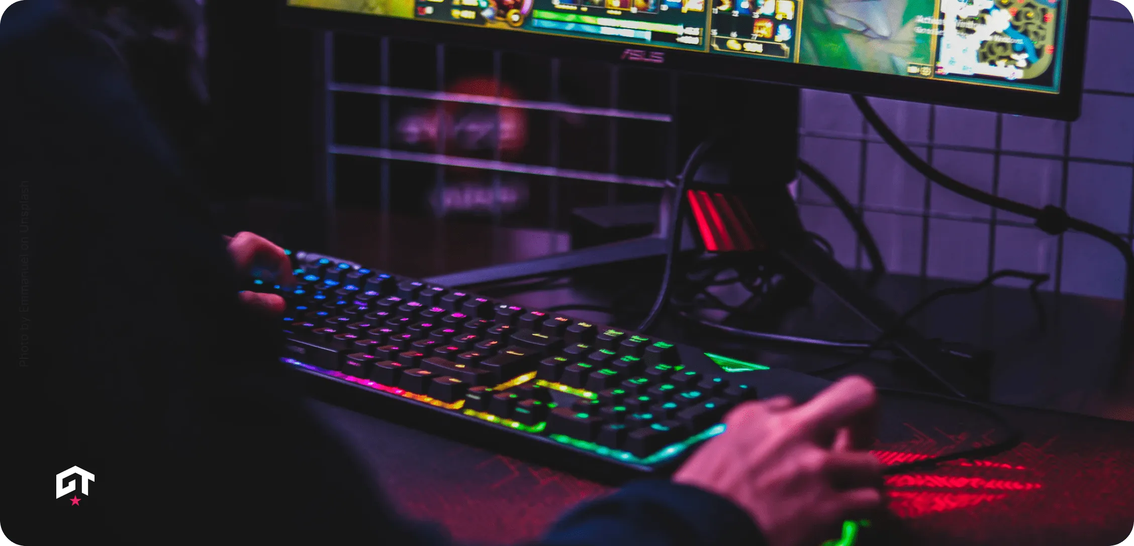 Person using a colorful RGB backlit keyboard and mouse while playing a video game on a widescreen monitor.