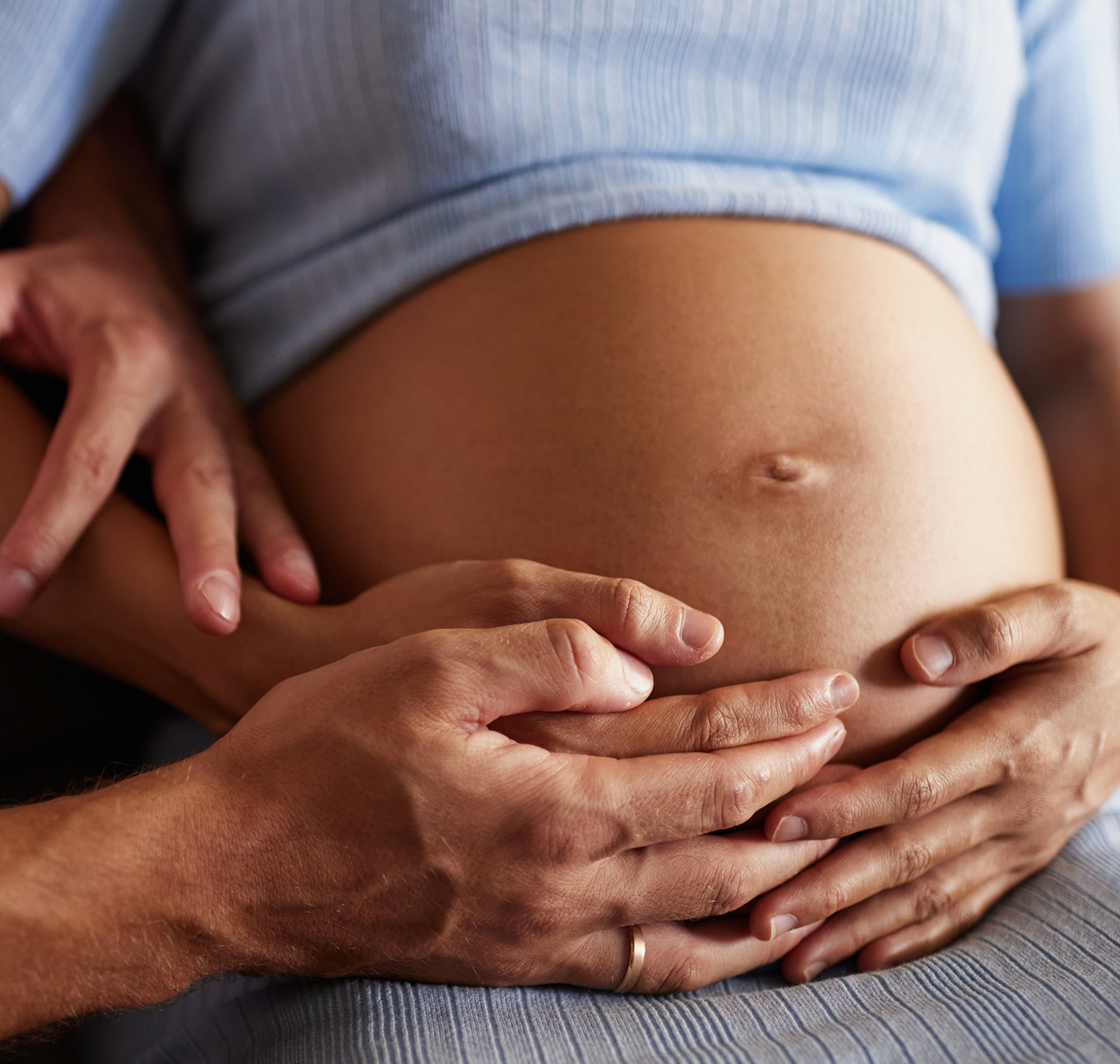 A partner's hands resting on a pregnant belly