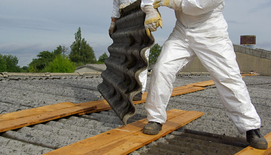 worker safely removing a panel of asbestos from roof while wearing hazardous materials protective equipment