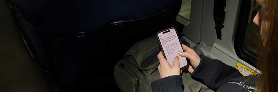Holding an iPhone on the bus, which is open to a notes app. The headline on the note reads "Things I learned about the strangers I sit next to on the bus by snooping at their phone"