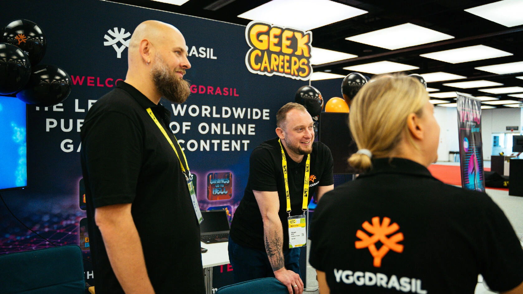 Three exhibitors at a trade show smiling and talking to an attendee