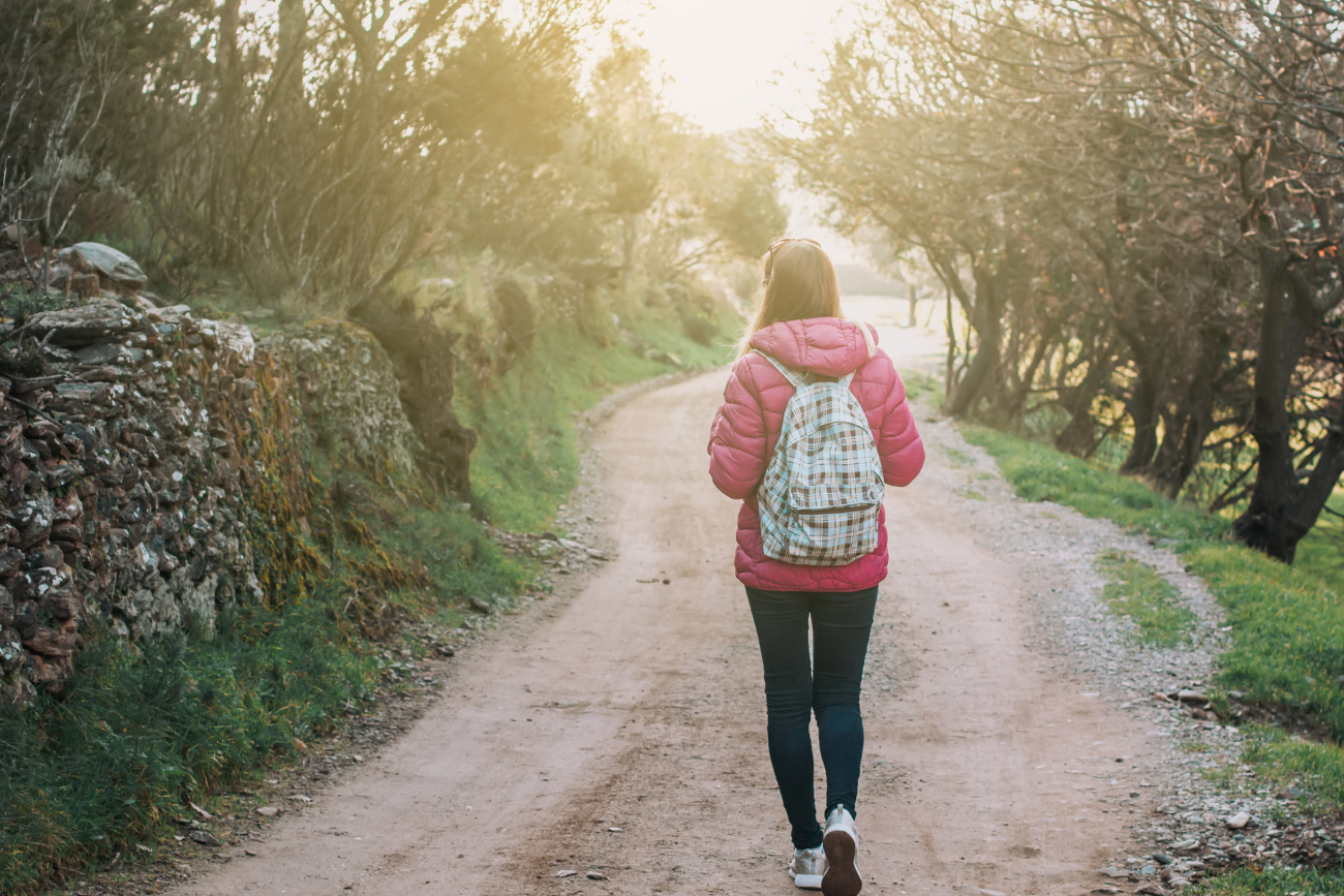 young woman with backpack walking on dirt path in forest