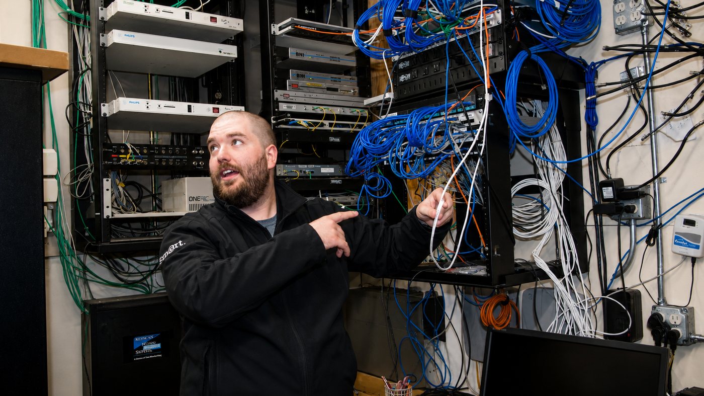 Smart Computers engineer tracing structured network cabling at a wall-mounted equipment rack in North Dakota