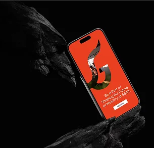 Smartphone displaying a red screen with a large G-shaped design and text reading 'Be a Part of Shaping the Future of Mobility at SSW.' The phone is positioned between two dark rocky surfaces against a black background.