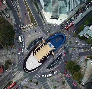 Aerial view of a city intersection with a large, digitally superimposed sneaker placed in the center, covering the roundabout and some surrounding roads and buildings.