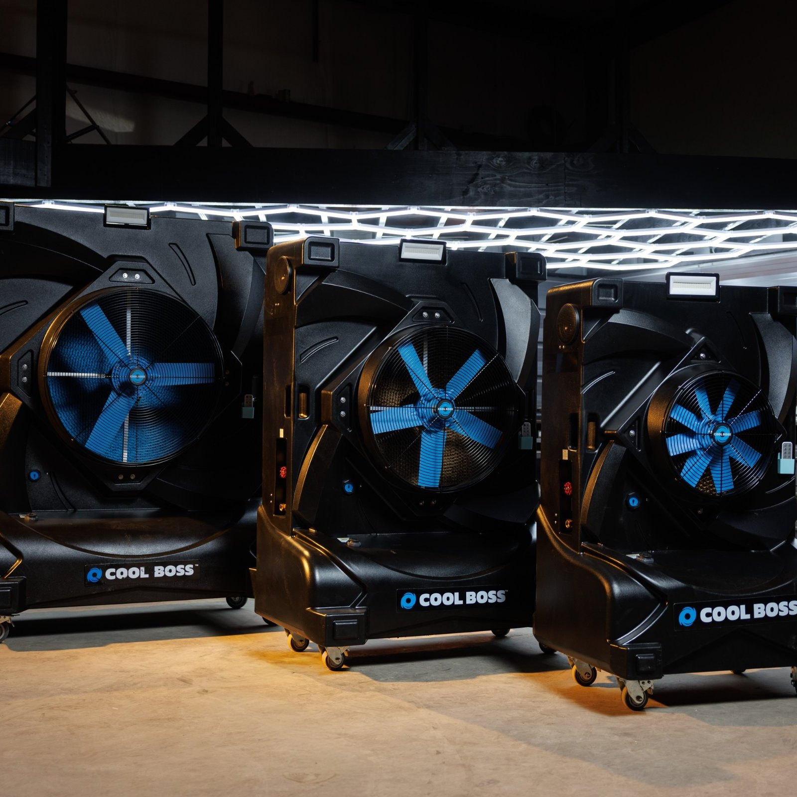 Three black Cool Boss evaporative coolers lined up in a garage under hex lighting