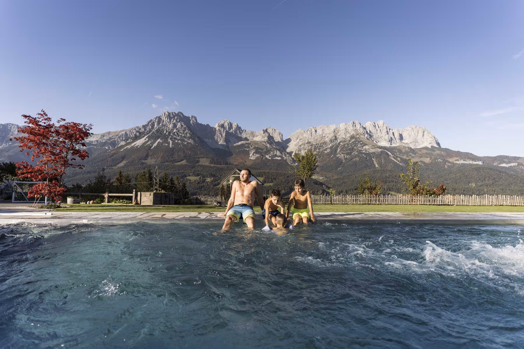 Vater sitzt mit Kindern an Beckenrand des Naschberghof-Pools.