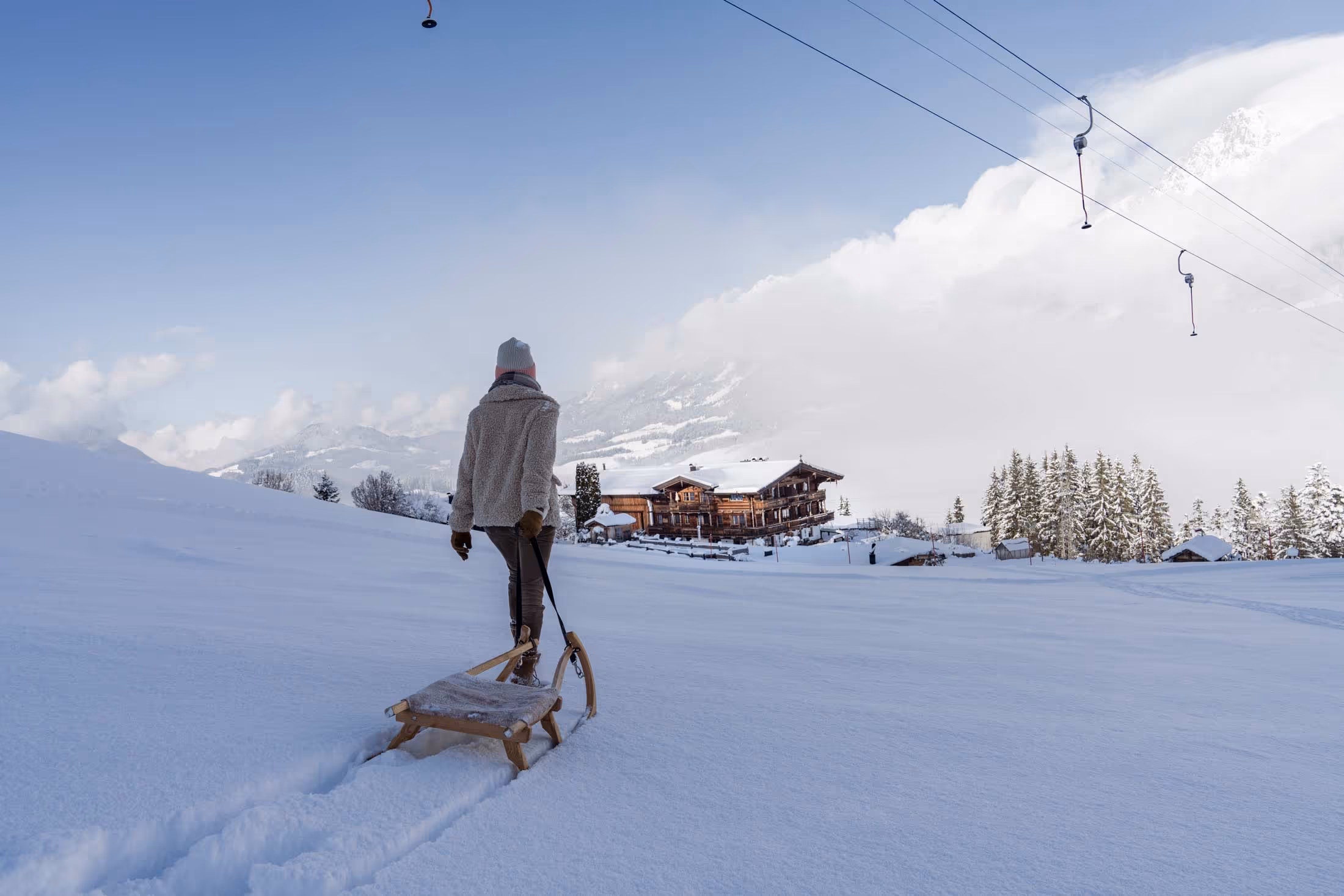 Frau kehrt von ihrer Rodelpartie zurück und zieht einen Schlitten durch den Schnee.