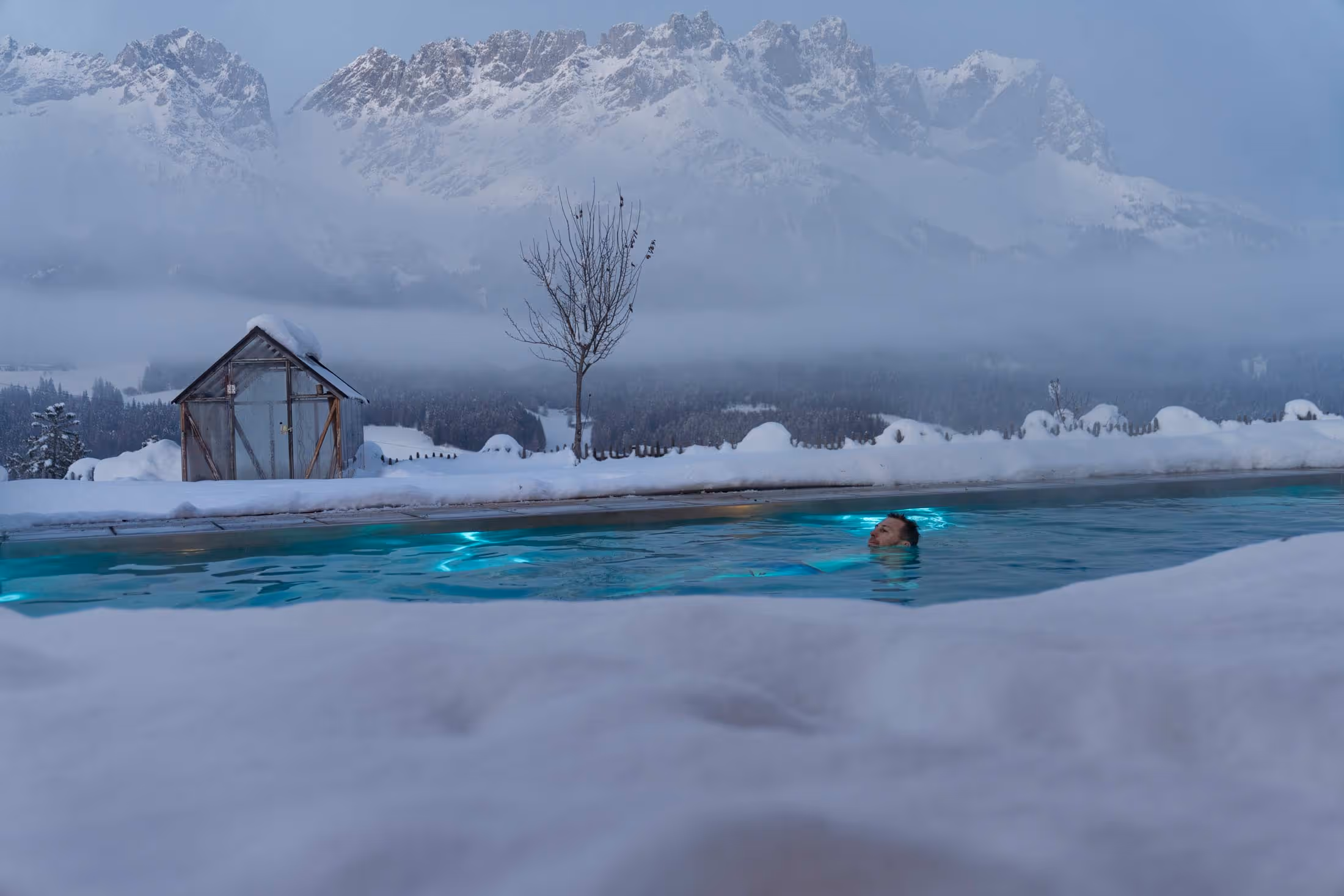 Ein Mann genießt das warme Wasser des Outdoor-Pools am Naschberghof.