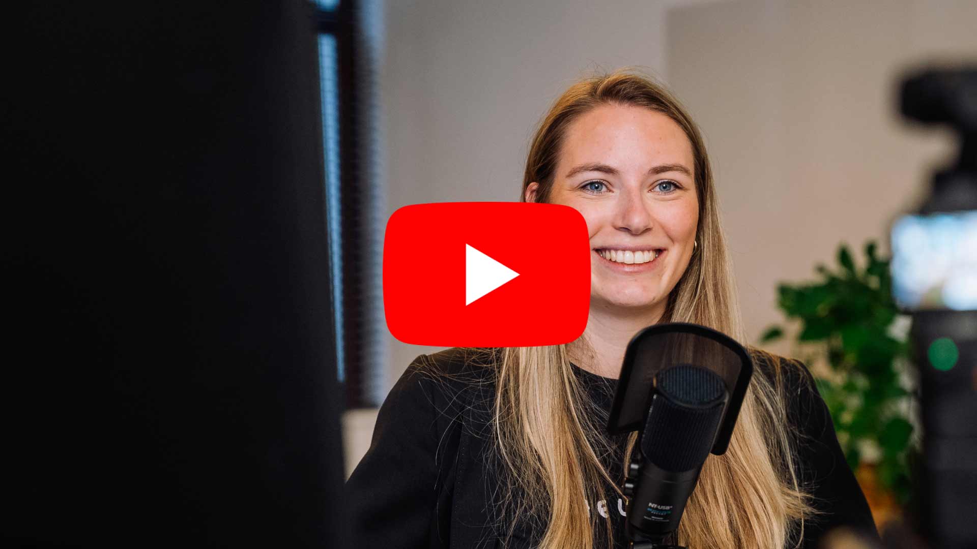 Eine junge Frau lächelt in die Kamera und spricht in ein Mikrofon, offenbar während einer Videoaufnahme oder eines Livestreams.