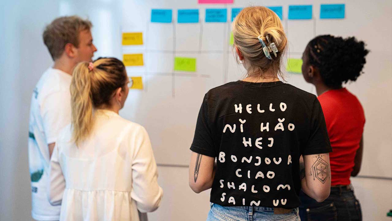 Vier Personen arbeiten gemeinsam an einem Whiteboard mit farbigen Haftnotizen, offenbar im Rahmen eines agilen Workshops.