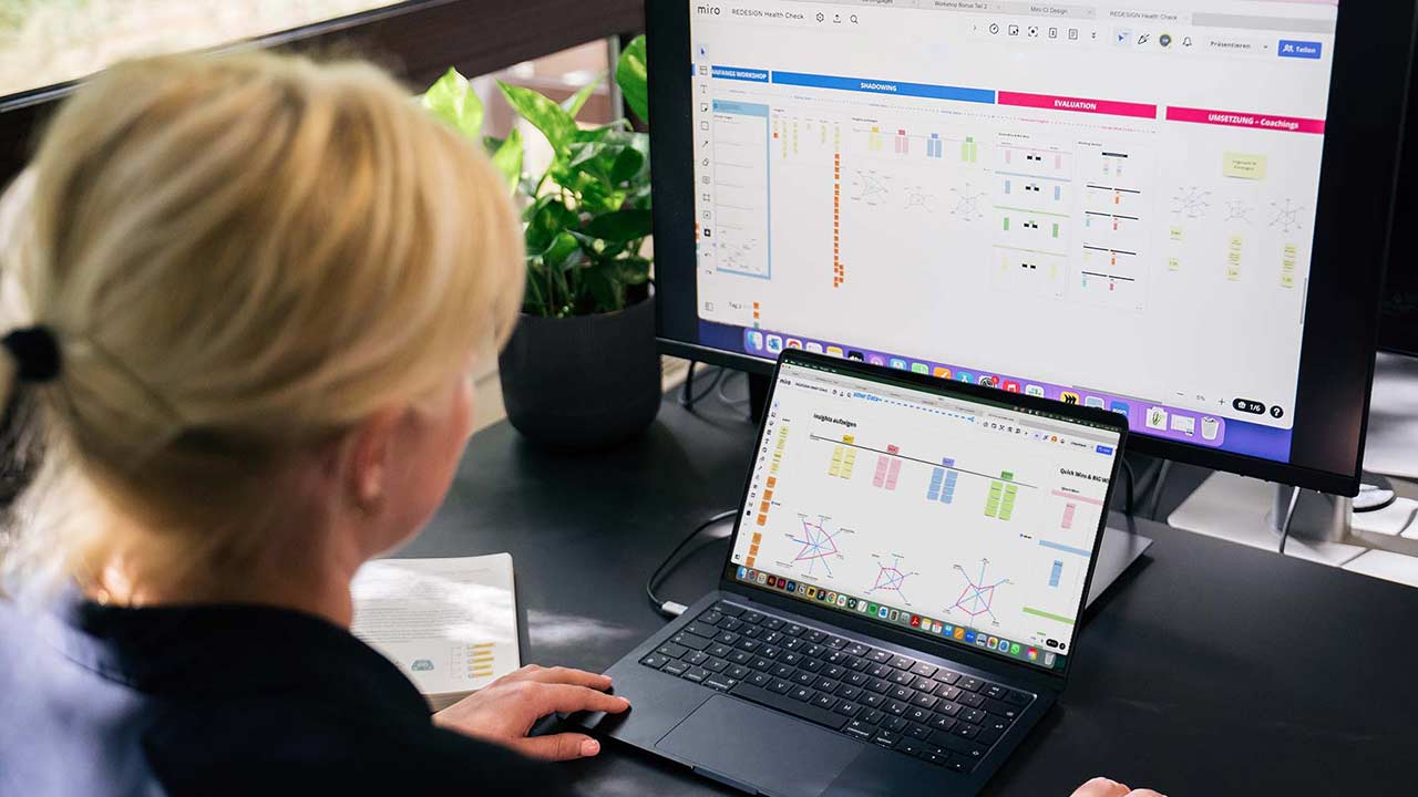Eine Frau arbeitet konzentriert an einem Laptop mit Diagramm-Software, während ein zusätzlicher Monitor die gleiche Anwendung zeigt.