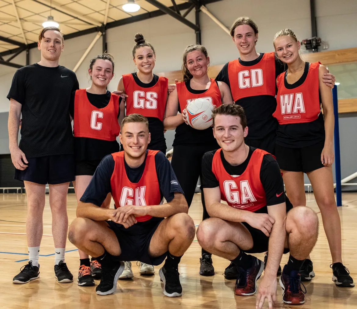 A mixed Netball team stand on the side of the court