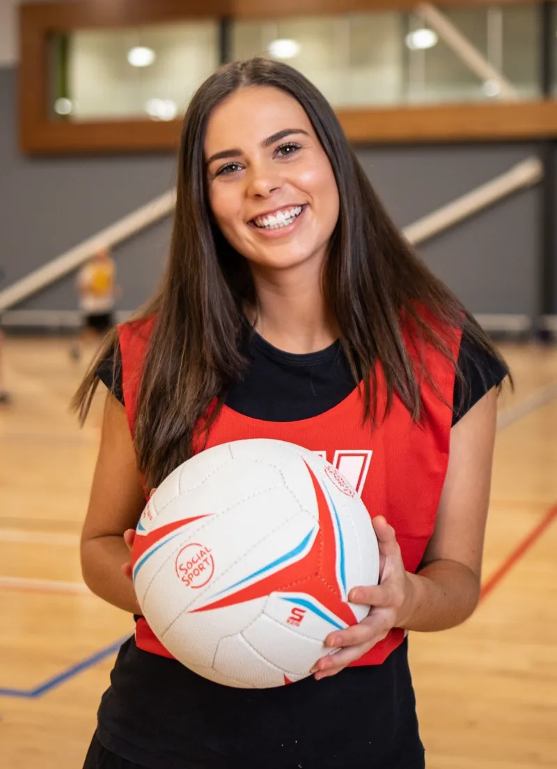 A female netball player smiles while holding the ball