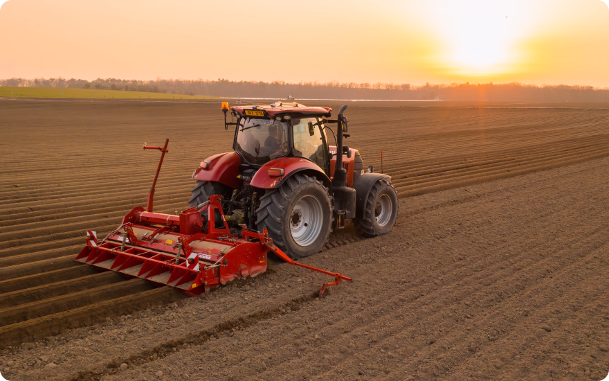 Red tractor, that is fuelled by rising oil prices, is tilling a farm field at sunrise.