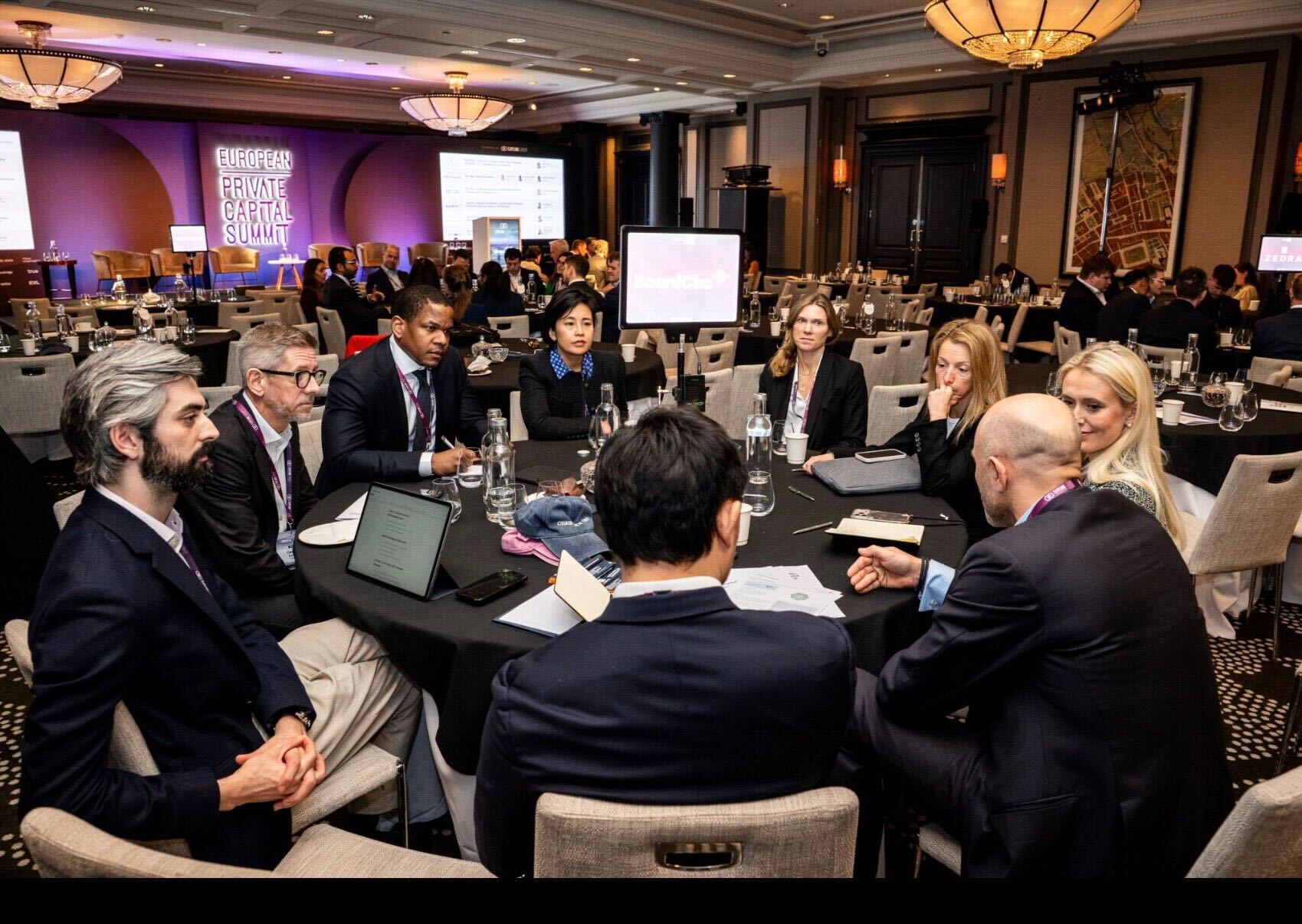Business professionals sitting around a roundtable at the European Private Capital Summit, engaged in discussion in a conference room.