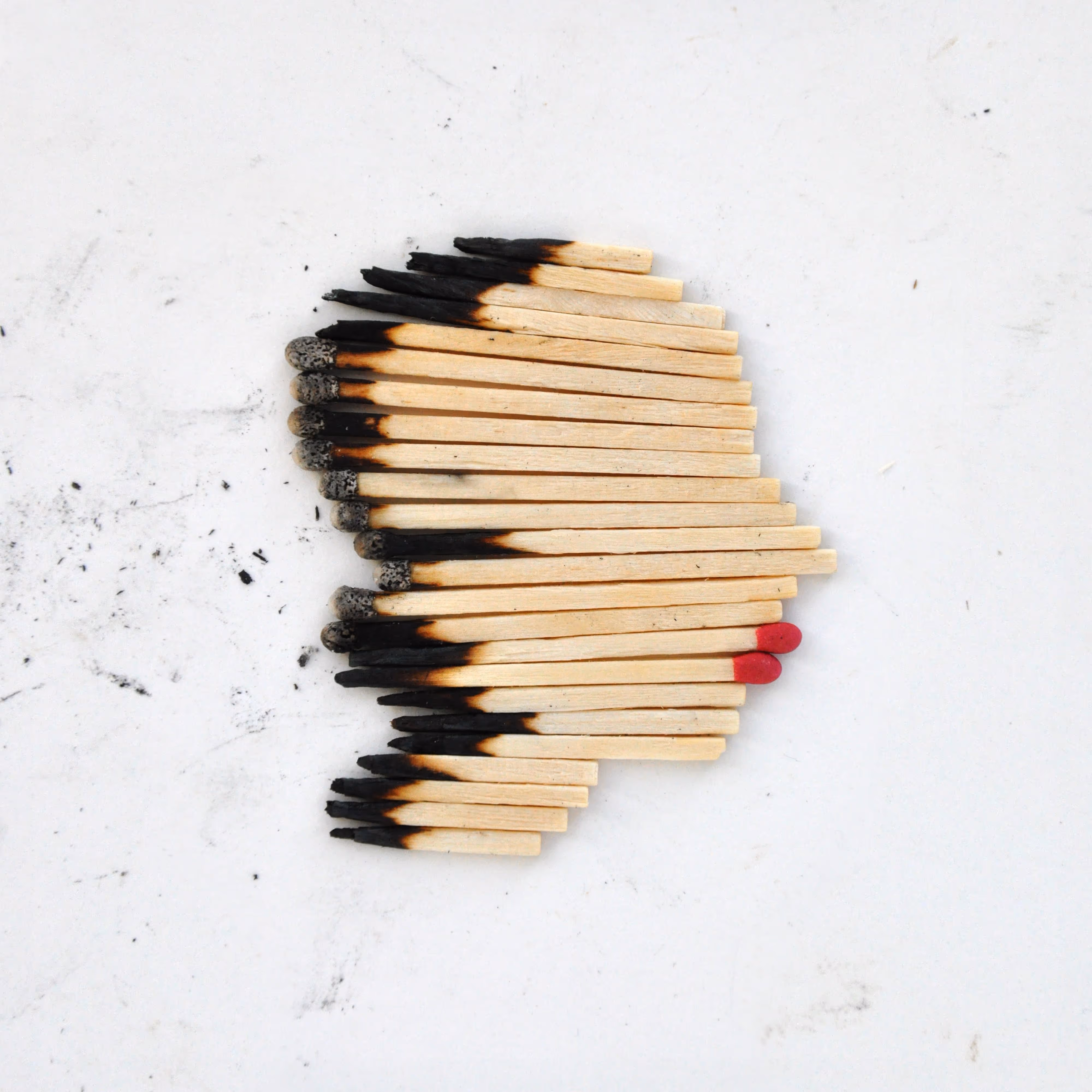 A silhouette of a human head made entirely of matchsticks with burnt ends on one side and bright red lips from the match heads 