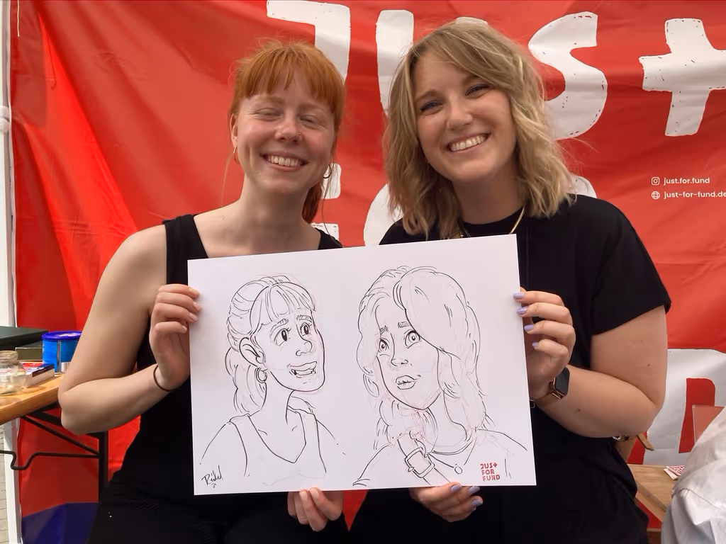 Zwei Frauen heben ein Plakat hoch, auf dem sie von Julian Reichel gezeichnet wurden.