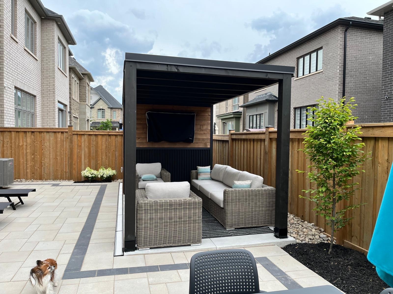 Modern cabana with black and wood-paneled walls, glass door, and a shaded patio area with outdoor seating beside a pool.