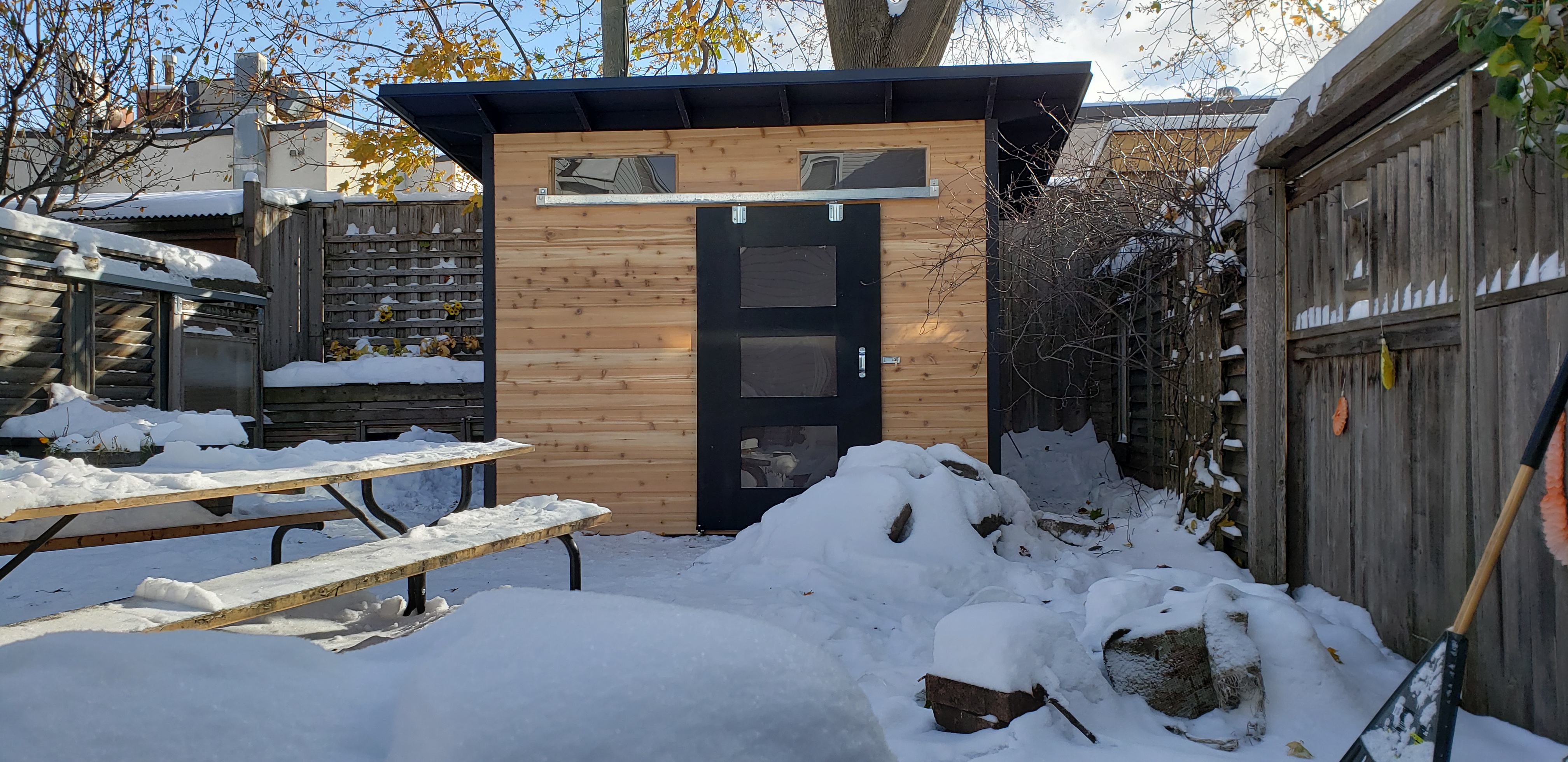 0x8 Advanced Shed installed in an Ottawa Ontario backyard in winter showing cedar front siding, black barn door with frosted windows, exposed rafter roofline, and jet black flashing and trim