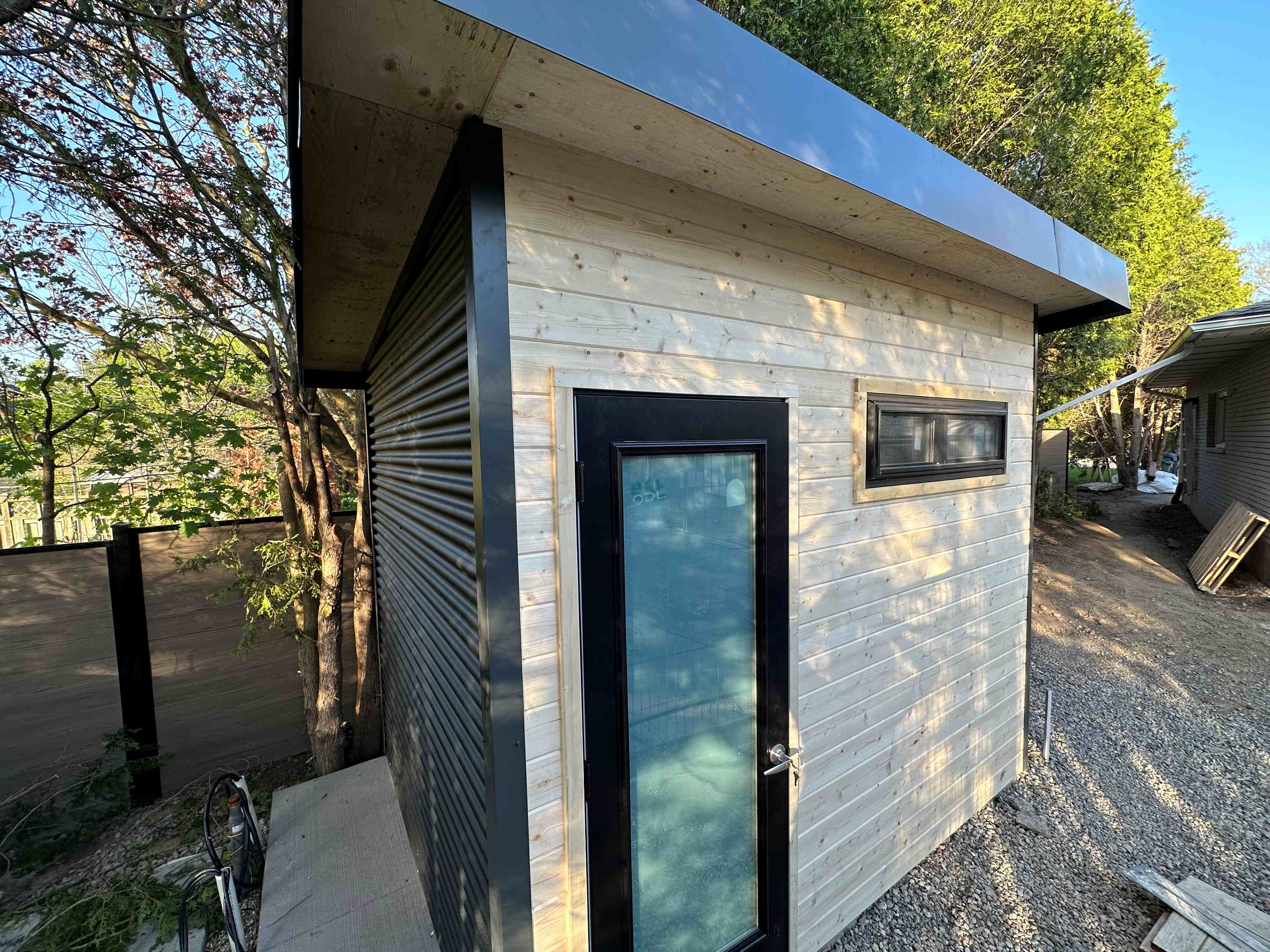 10x7-suburban-shed-guelph-ontario-pine-front-frosted-glass-door.jpg Alt text: Angled front view of 10x7.5 Suburban Shed with natural pine horizontal siding, full-glass frosted door, frosted slider window, and Iron Ore steel column in Guelph Ontario by Back