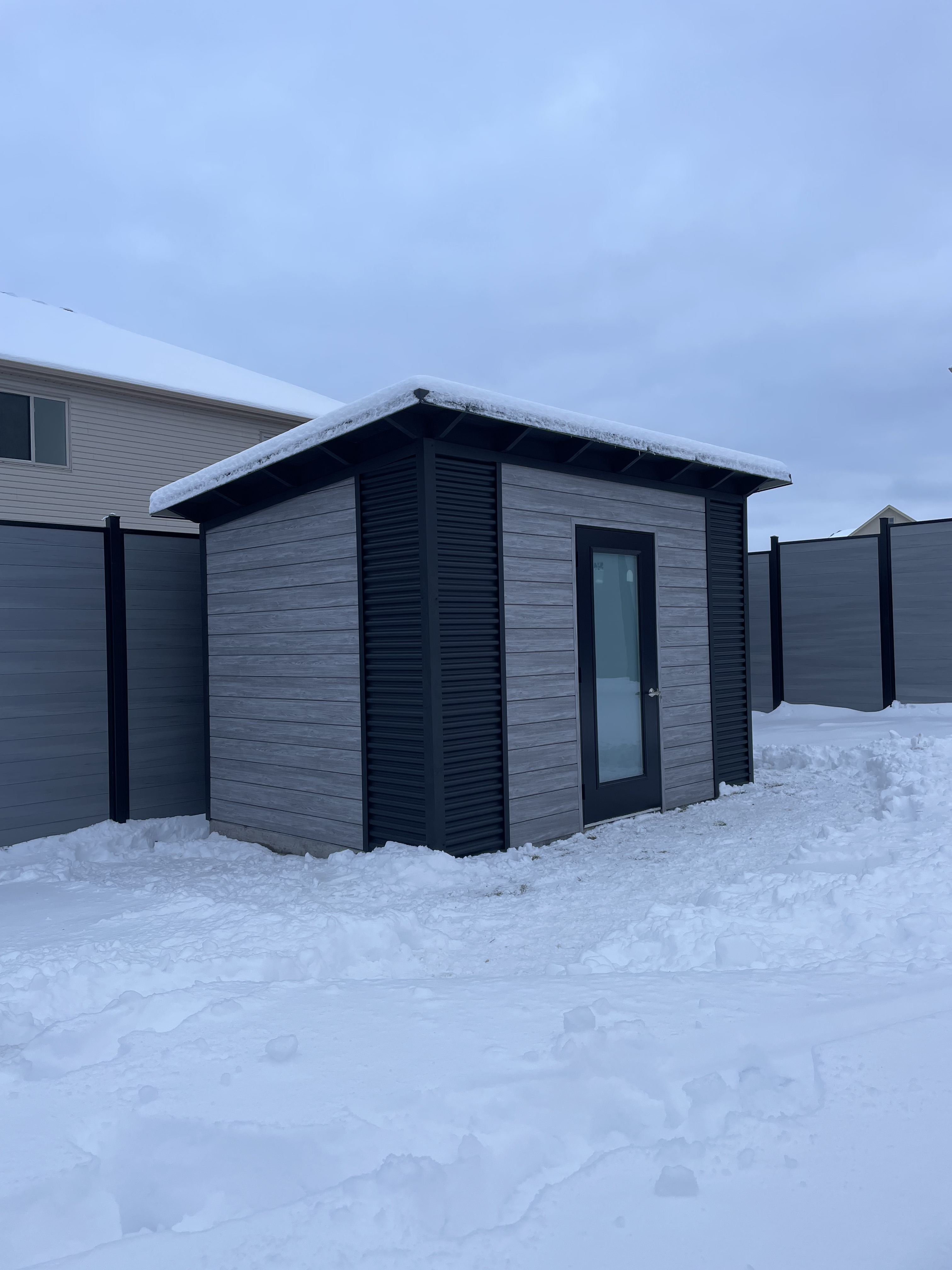 12x8 Essential Shed with Barnboard Grey Chamclad shiplap siding, black corrugated steel corner accents, and full frosted glass outswing door in Kitchener Ontario, installed by Backyard Escape Studios.