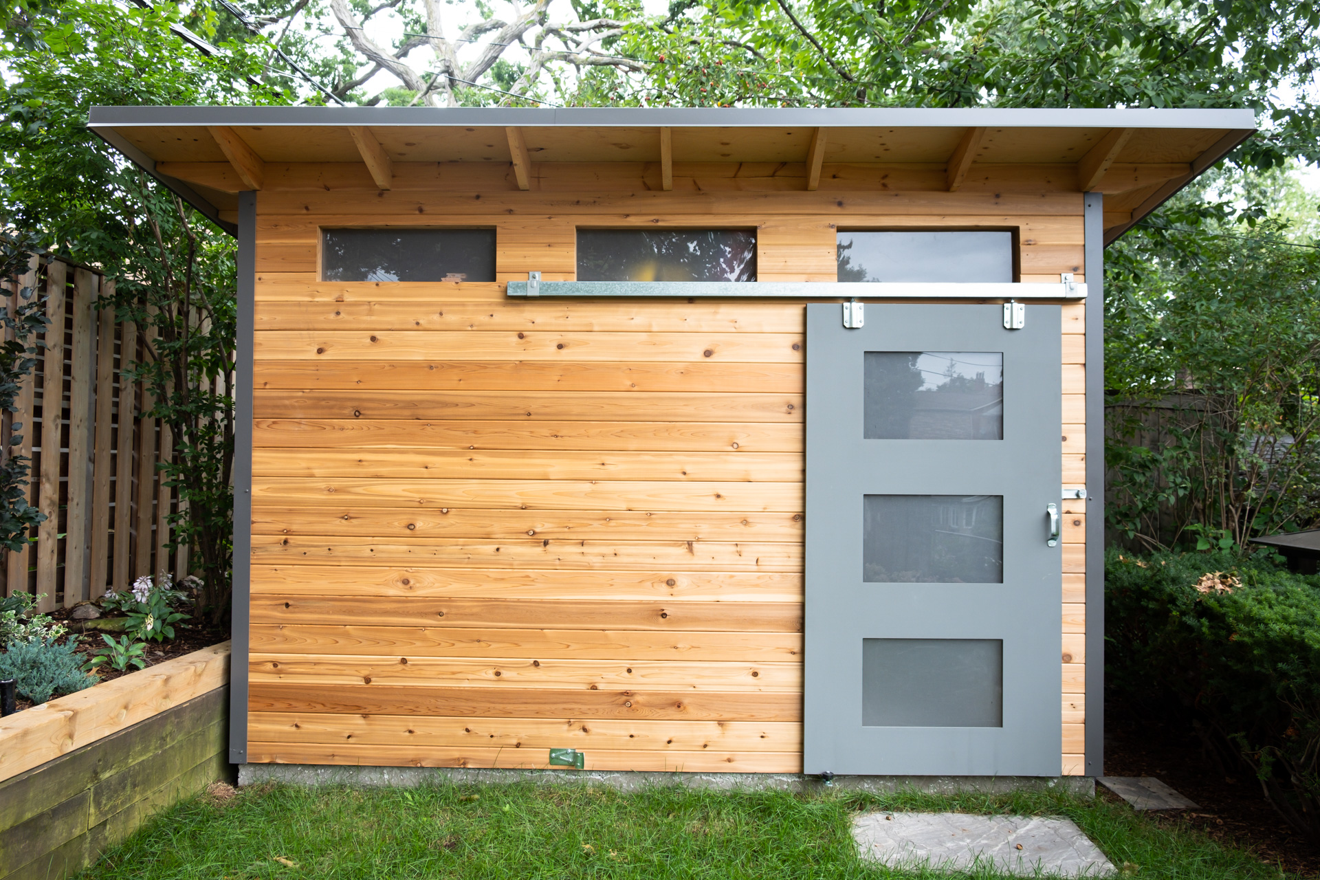 Front elevation of 12x8 Advanced Shed in Toronto Ontario with horizontal Western Red Cedar T+G wall and Kendall Charcoal sliding barn door with frosted glass panels, installed by Backyard Escape Studios.