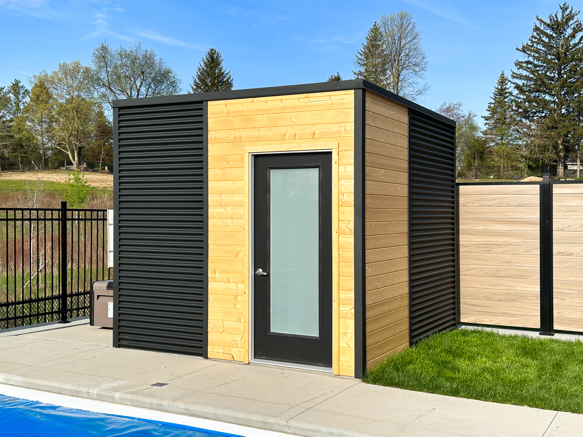 10x9.5 Cube Shed pool shed with jet black corrugated steel and raw pine walls viewed from front angle, installed poolside in Kitchener Ontario by Backyard Escape Studios.