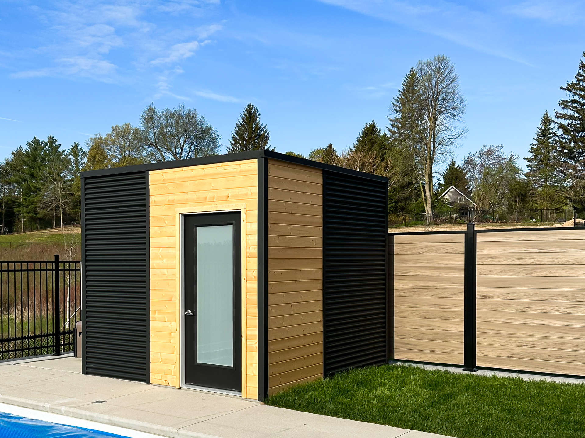 10x9.5 Cube Shed pool shed with frosted glass inswing door and split steel and pine exterior beside an inground pool in Kitchener Ontario, built by Backyard Escape Studios.