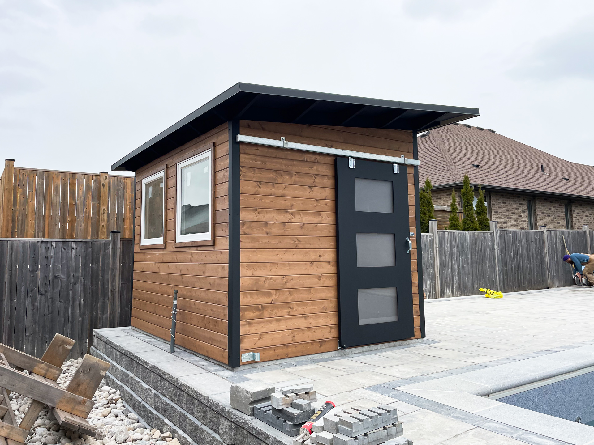 Close view of 10x8 Advanced Shed front wall in Strathroy Ontario featuring horizontal cedar T+G panelling in Muskoka Brown stain and Black Beauty sliding barn door with frosted glass, installed by Backyard Escape Studios.