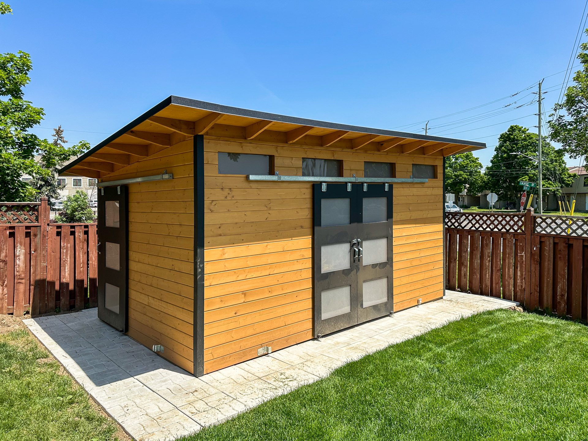 16x10 Advanced Shed with cedar stain pine siding, Jet Black corrugated steel, and double sliding barn doors with frosted glass installed in Georgetown Ontario by Backyard Escape Studios.