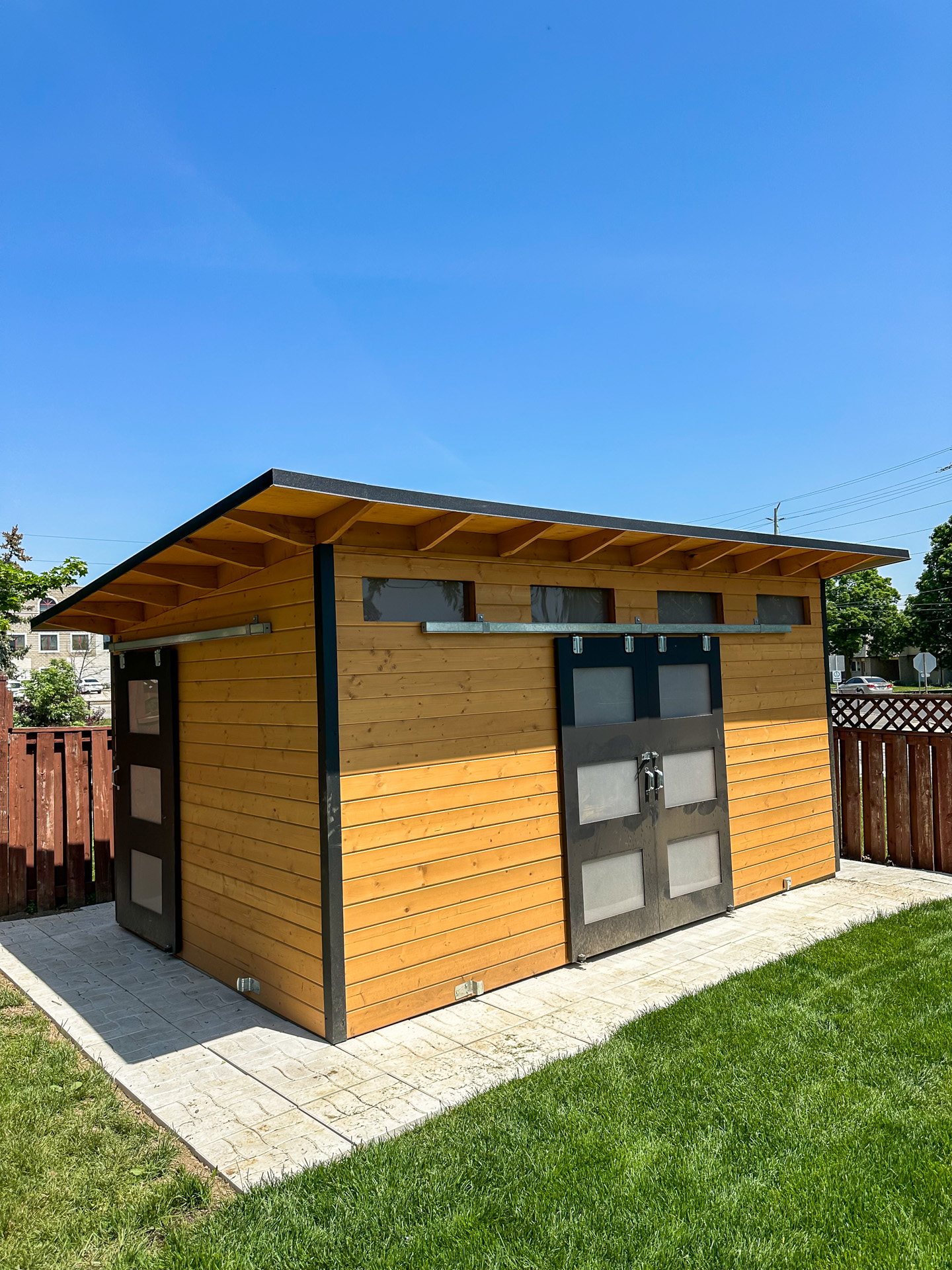 16x10 Advanced Shed with Muskoka Brown cedar stain pine siding and double sliding Black Beauty barn doors with frosted Lexan glass in Georgetown Ontario, installed by Backyard Escape Studios.