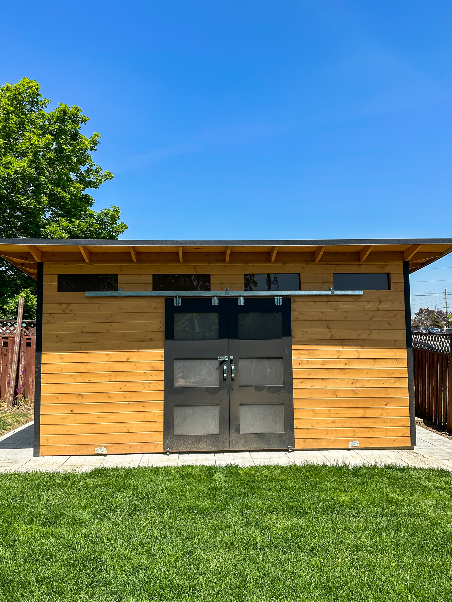 Front elevation of 16x10 Advanced Shed in Georgetown Ontario showing double sliding barn doors, four transom windows, and cedar stain pine T+G wall, installed by Backyard Escape Studios.