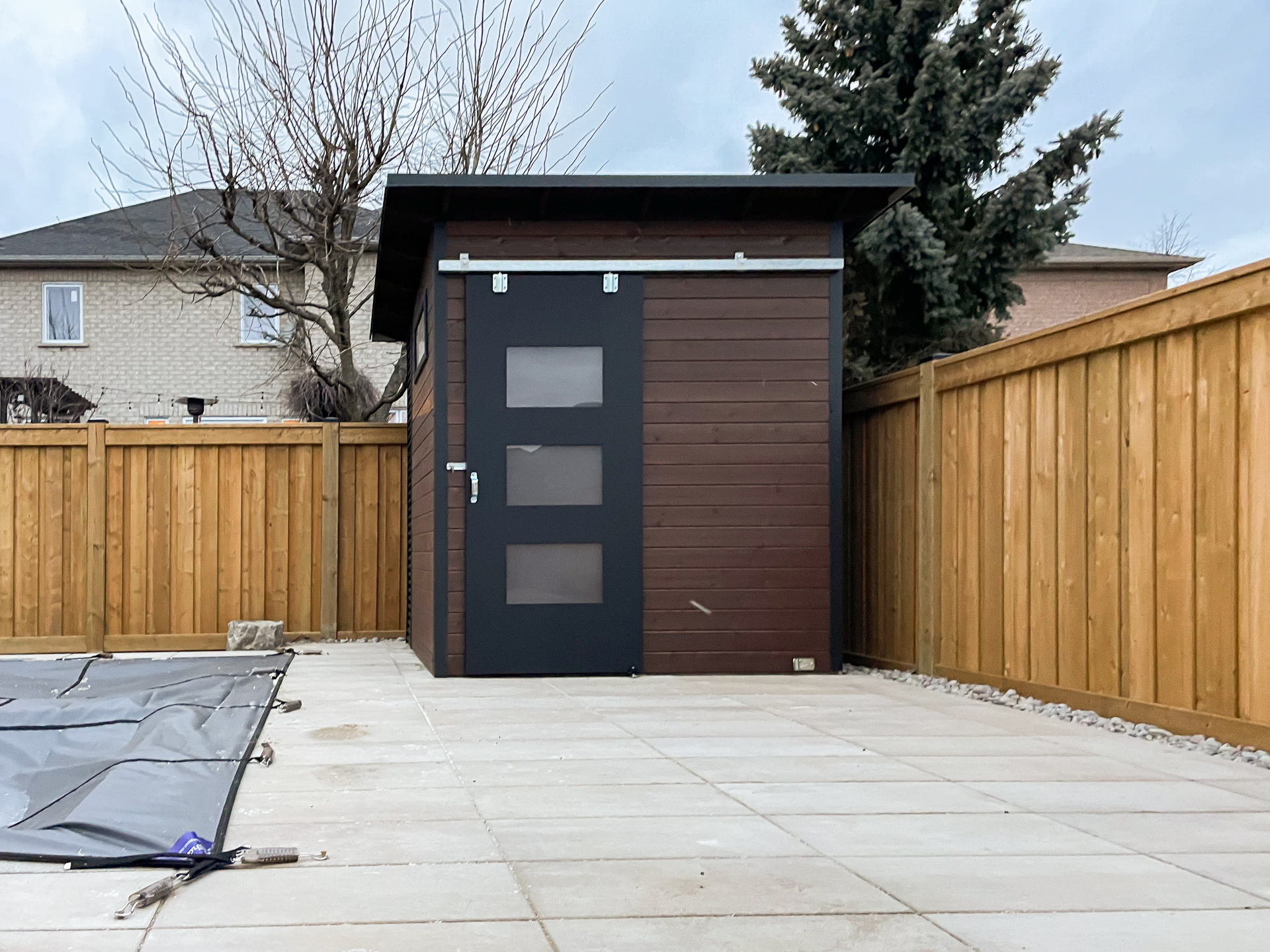 Side-angle view of 8x8 Essential Shed in Maple Ontario showing Jet Black corrugated steel left wall, frosted Lexan transom window, and Black Beauty sliding barn door hardware by Backyard Escape Studios.