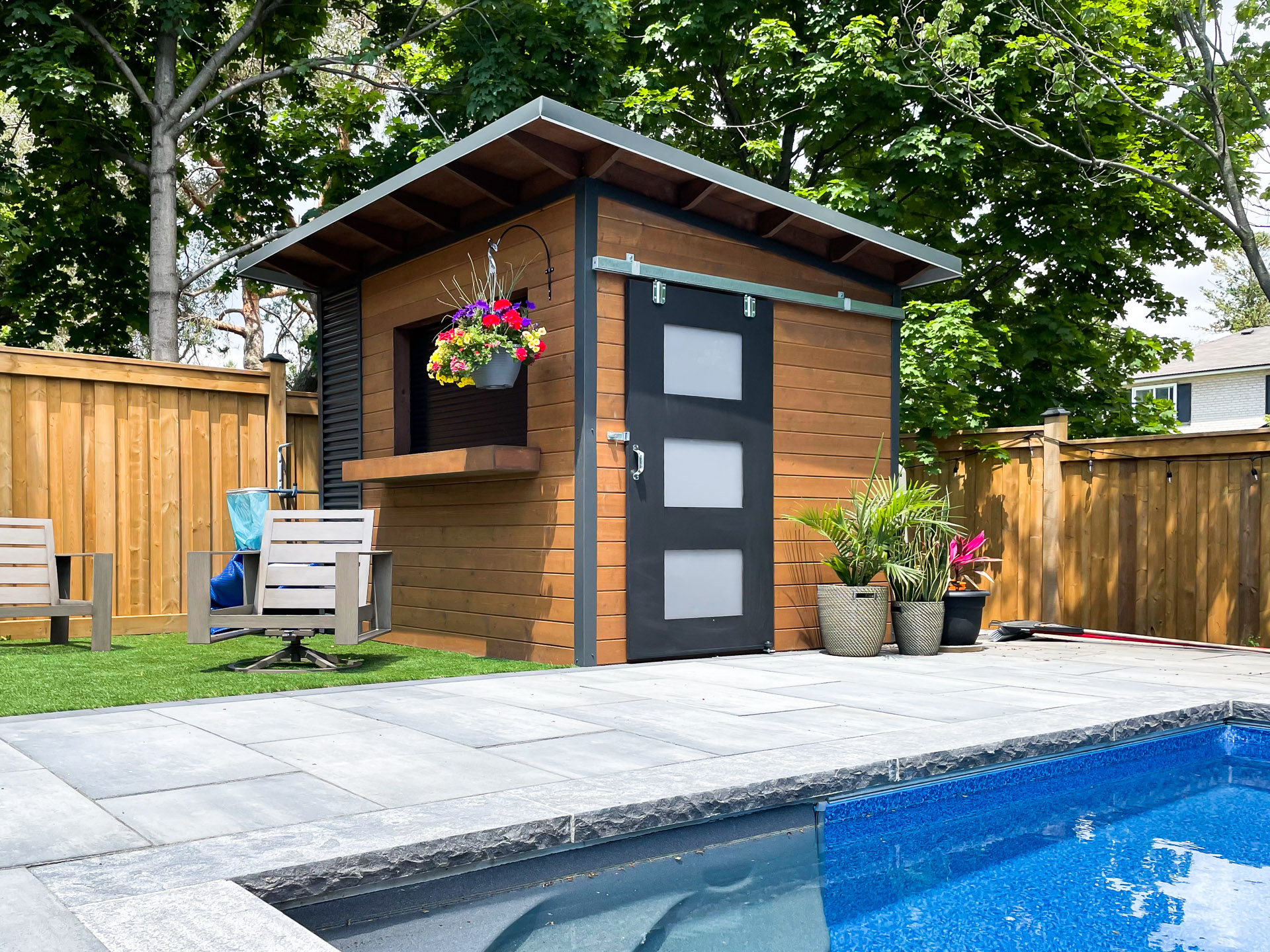 10x8 Essential pool shed with charcoal corrugated steel siding, stained pine T+G panelling, roll-up bar window, and sliding barn door in North York Ontario, installed by Backyard Escape Studios.