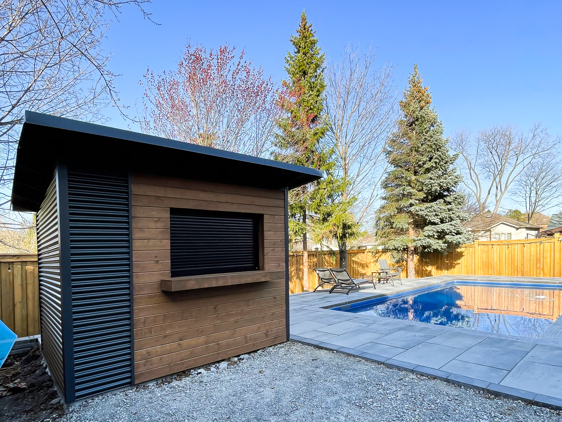 10x8 Essential pool shed with charcoal corrugated steel siding on the back and side walls, viewed from across the pool deck in North York Ontario, installed by Backyard Escape Studios.