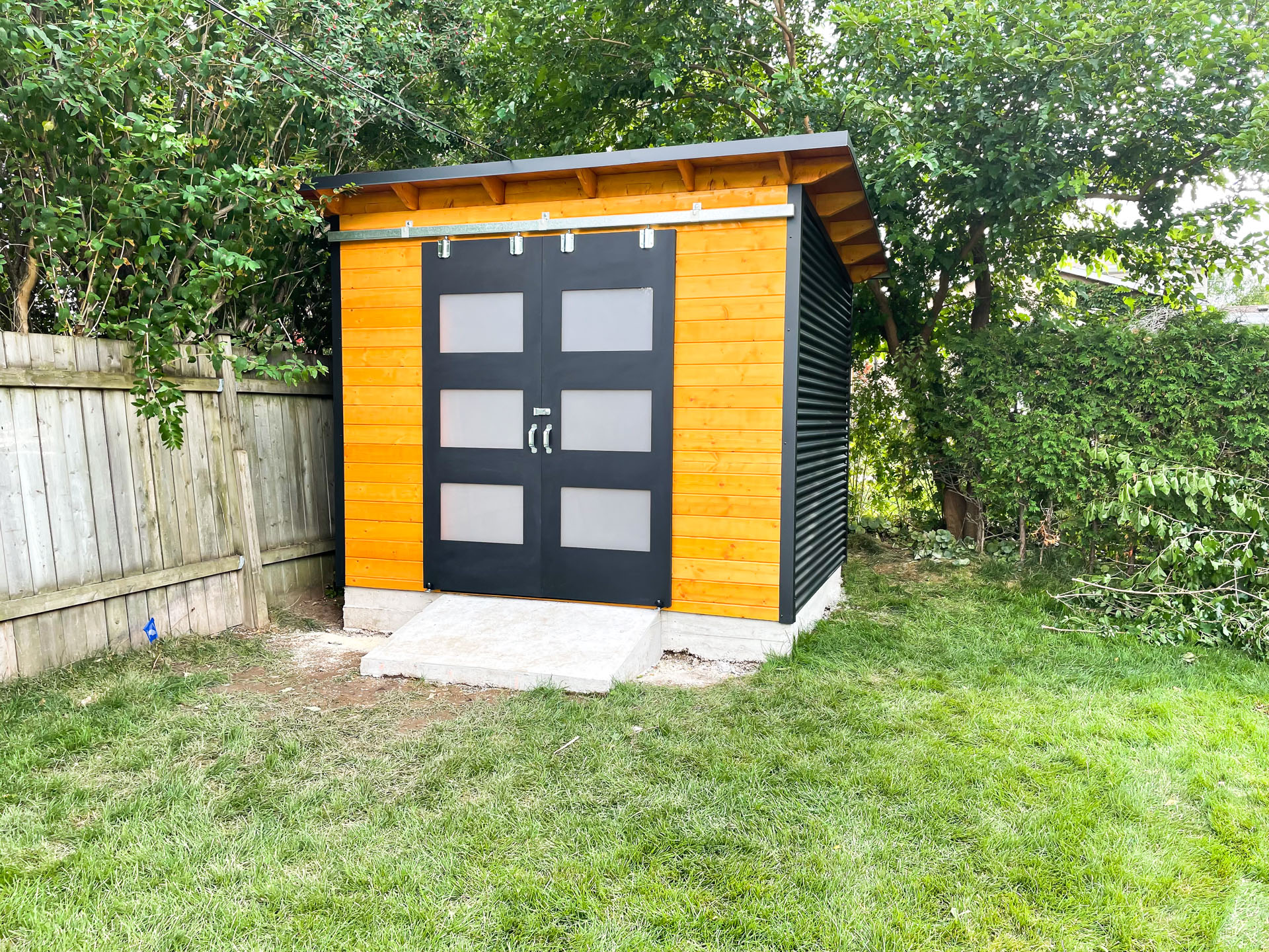 Front view of 10x8 Essential Shed in Burlington Ontario showing double sliding barn doors with frosted Lexan glass panels and Muskoka Brown stained pine wall, installed by Backyard Escape Studios.