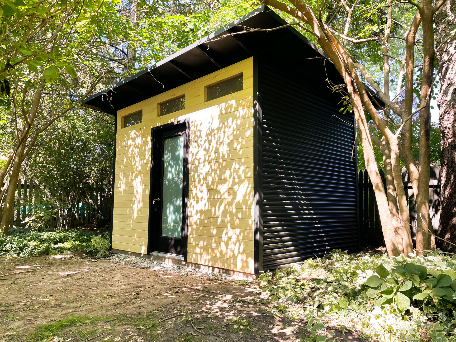 12x9 modern shed with jet black steel siding and black cap sheet roof installed in a wooded backyard in Blue Mountains Ontario by Backyard Escape Studios.