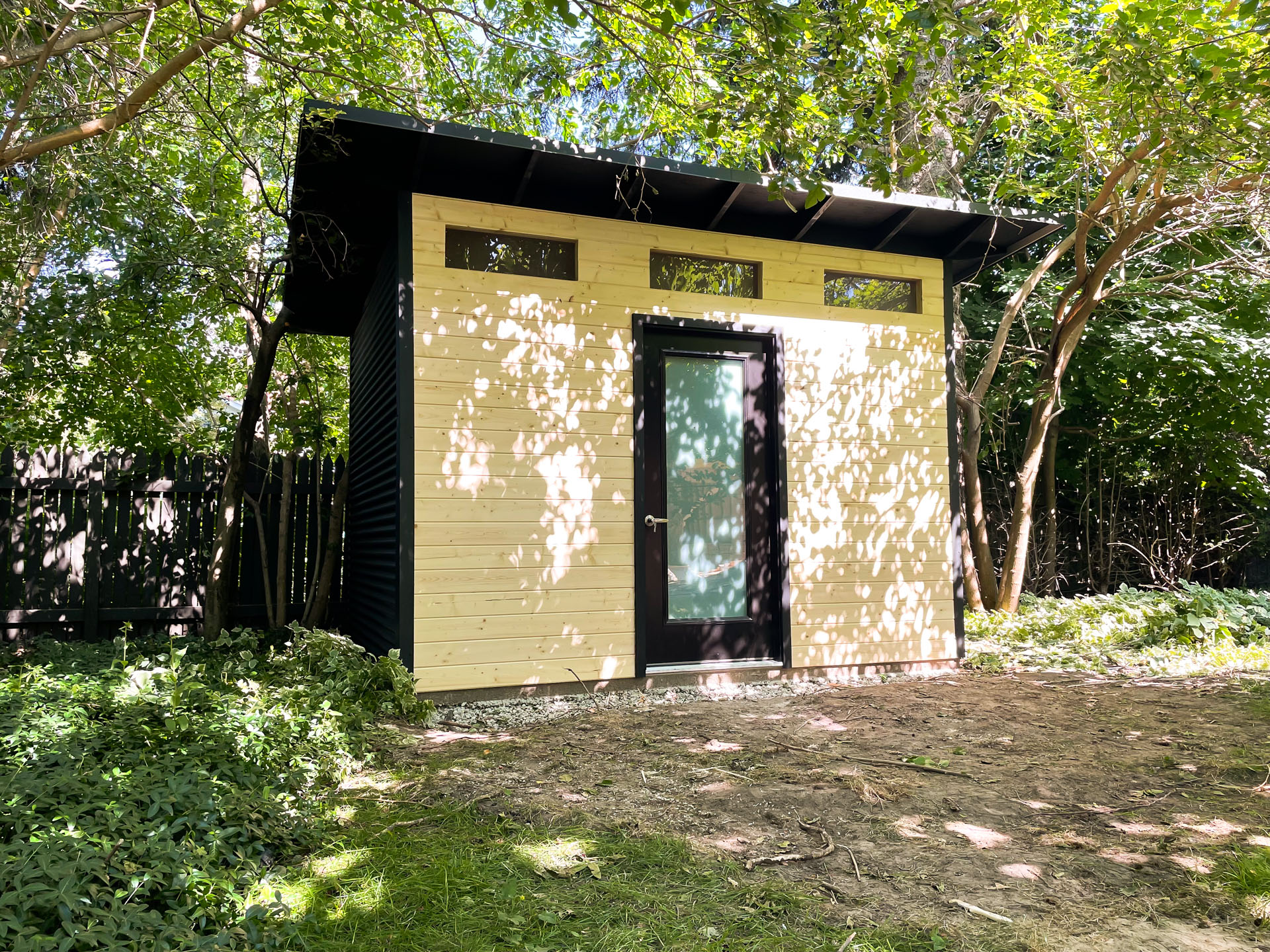 Front view of 12x9 modern shed in Blue Mountains Ontario showing three transom windows and a frosted full-glass inswing door on a pine tongue-and-groove front wall.