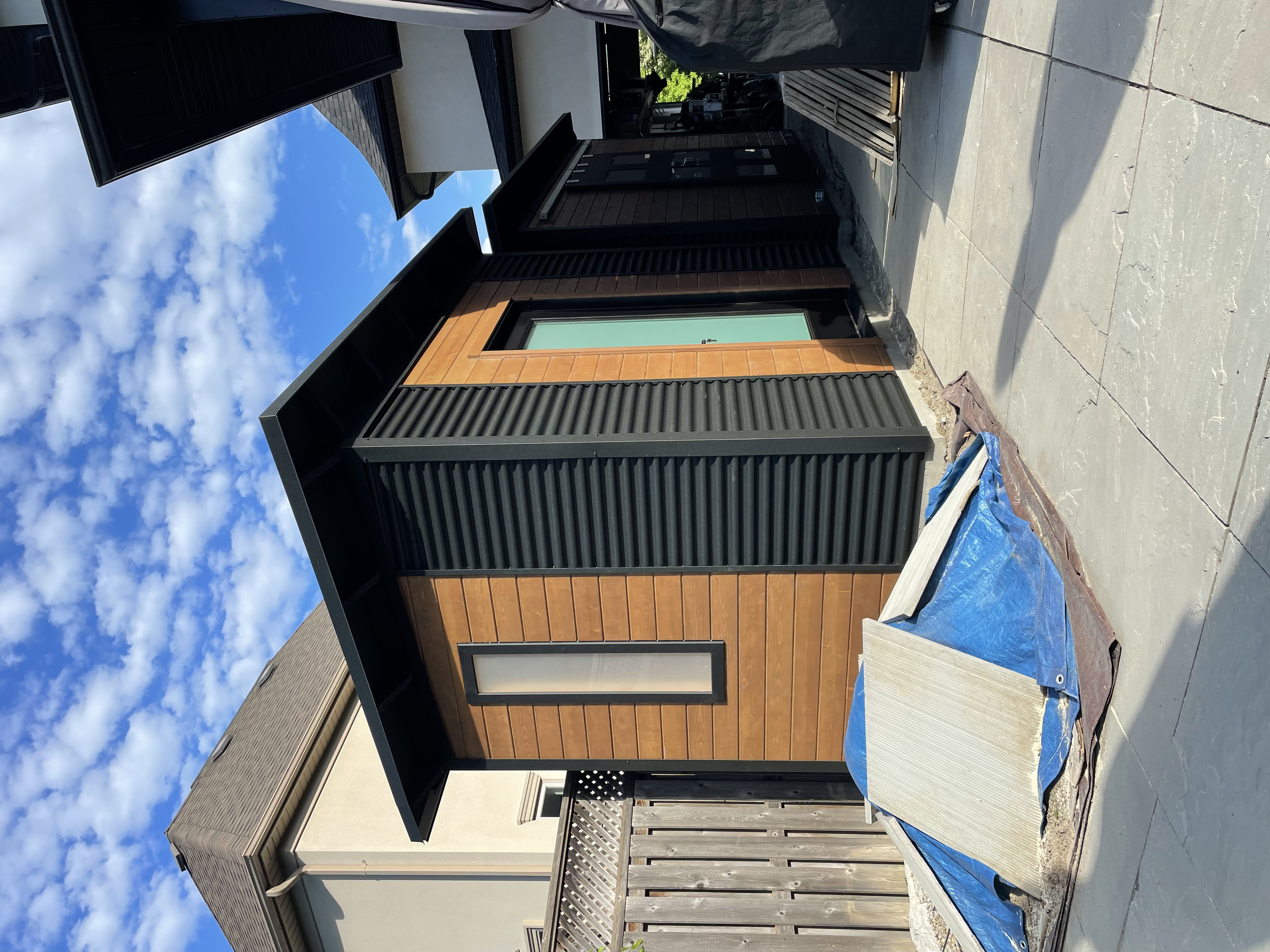 Two matched Essential Sheds with Jet Black corrugated steel siding and Muskoka Brown horizontal pine T+G front walls installed side by side in Etobicoke Ontario by Backyard Escape Studios.