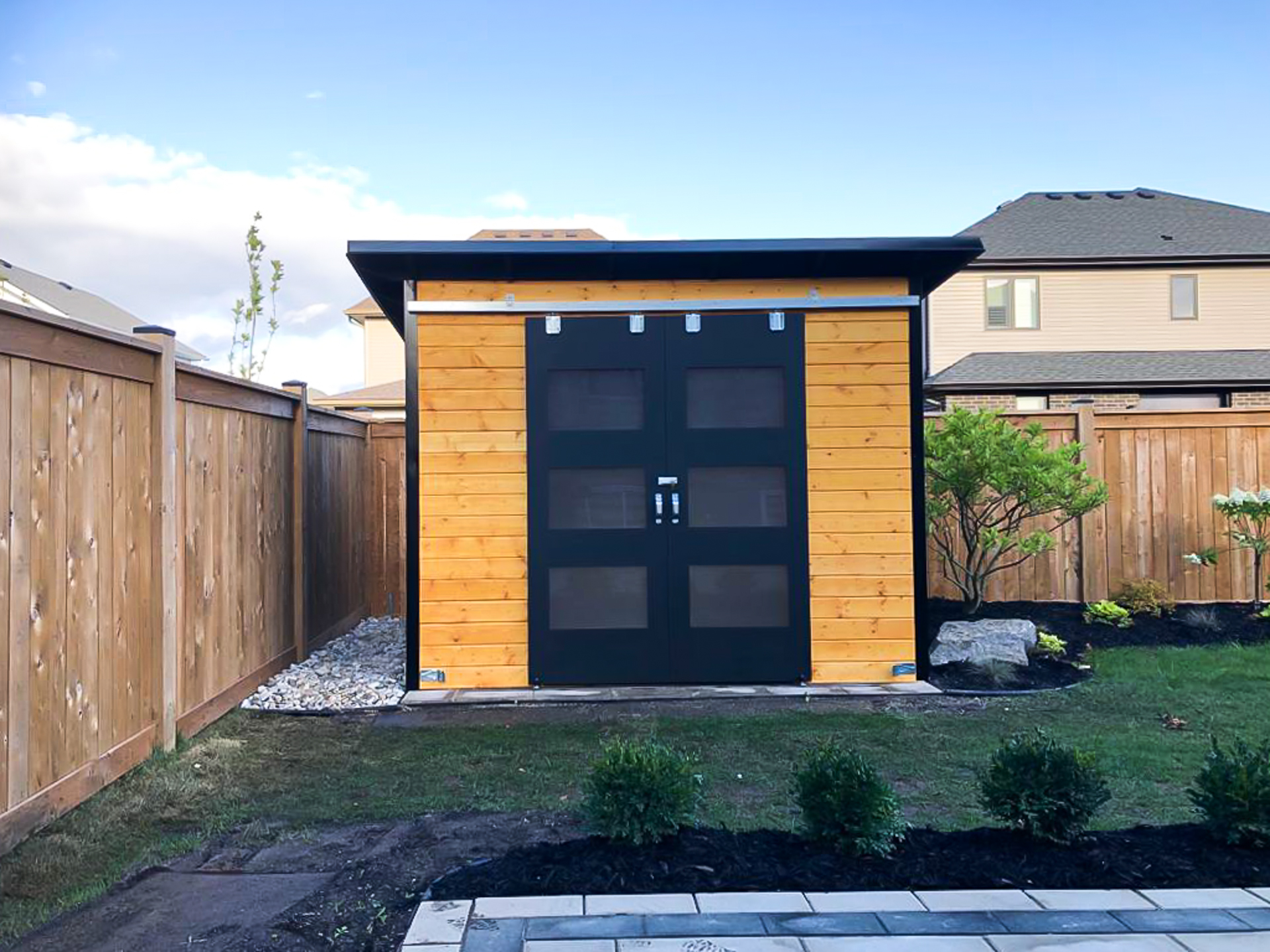 10x8 Essential Shed with classic black corrugated steel siding, cedar stain pine front wall, and double sliding barn doors with frosted glass, installed in St. Thomas Ontario by Backyard Escape Studios.